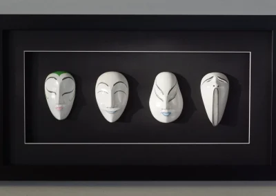 Quatre masques japonais en bois alignés dans un encadrement boîtier noir