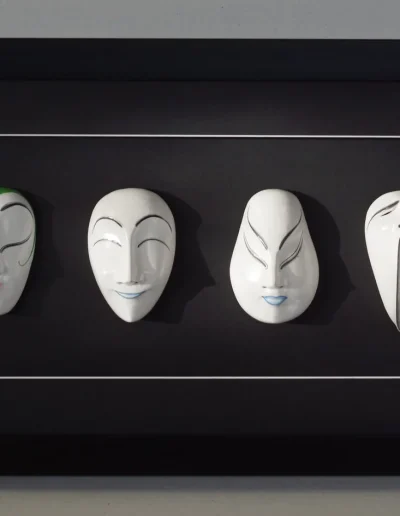 Quatre masques japonais en bois alignés dans un encadrement boîtier noir