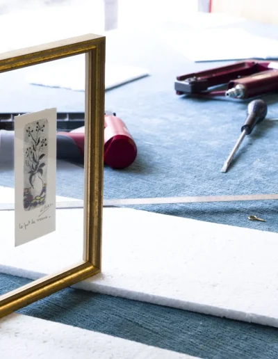 Encadrement entre deux verres, cadre doré posé sur l'établi de l'Atelier Valette au milieu des outils