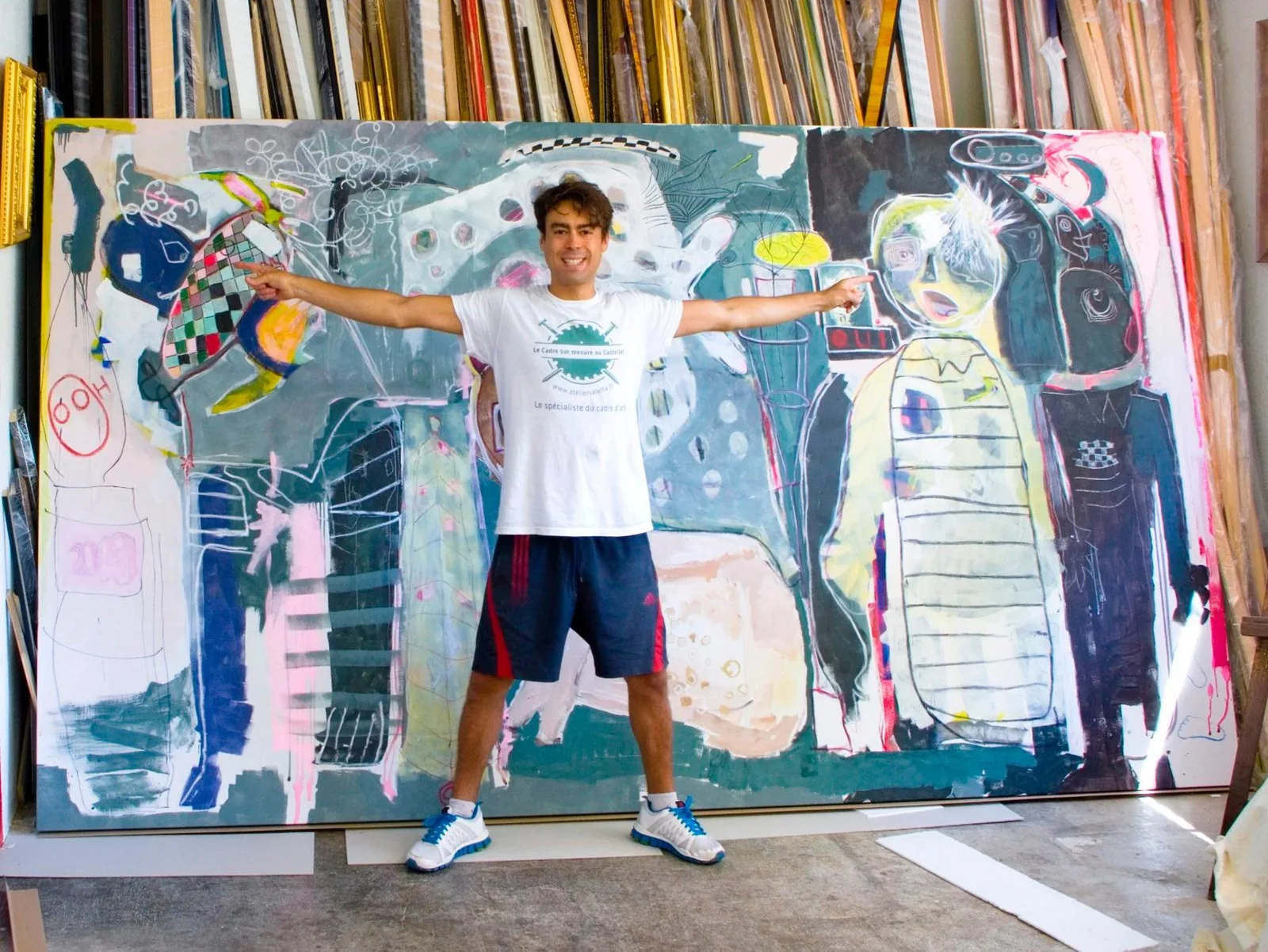 Julien Silvestro, encadreur d'art, bras écartés devant une toile de grand format en cours d'encadrement