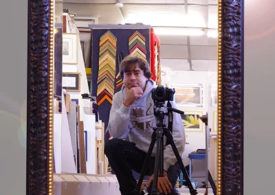 Miroir encadré d'un profil prune sculpté à filet doré, reflétant l'intérieur de l'atelier